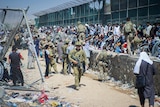 Soliders patrol as swathes of people congregate along a wall.