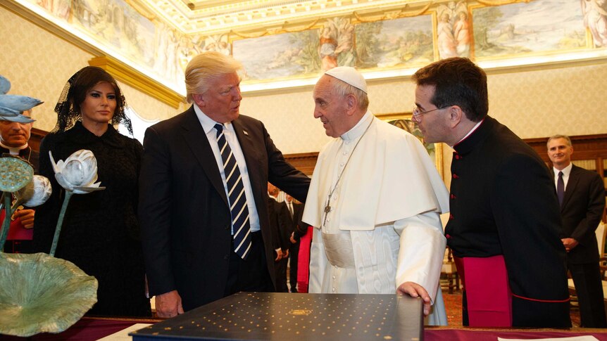 Donald trump with his arm around Pope Francis as the pontiff holds the holy book in front of them and Melania Trump looks on.