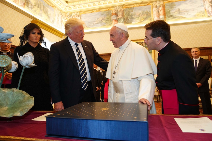 Donald trump with his arm around Pope Francis as the pontiff holds the holy book in front of them and Melania Trump looks on.