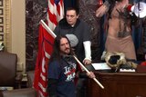 A man stands in the Us Senate with a flag and wearing a Trump t shirt