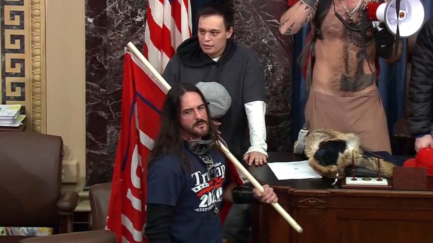 A man stands in the Us Senate with a flag and wearing a Trump t shirt