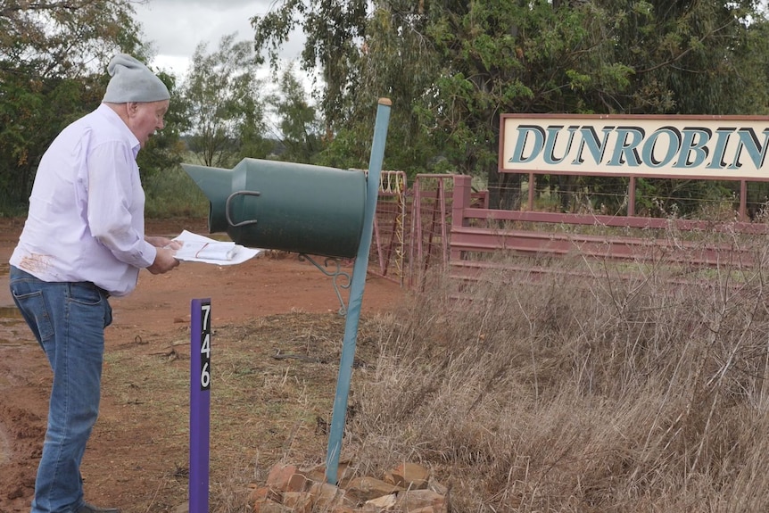 A man puts a letter in a letter box surrounded by trees.