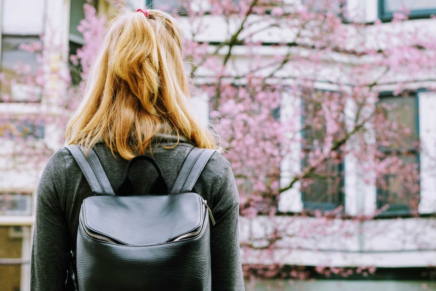 Woman with backpack looking at cherry blossoms and a building.