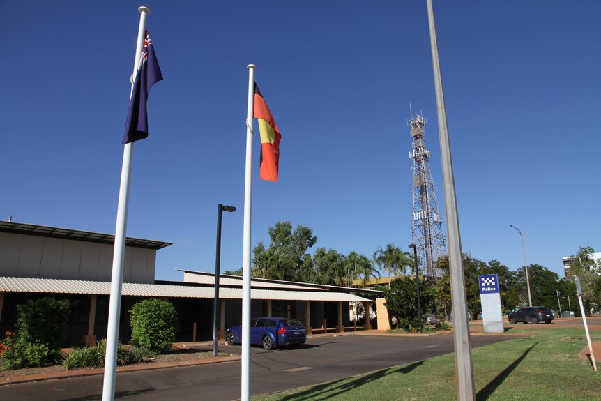 An Australian flag and Aboriginal flag fly in front of a police station with palm trees in the background