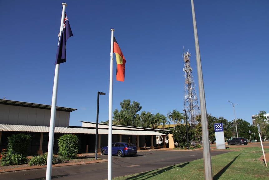 An Australian flag and Aboriginal flag fly in front of a police station with palm trees in the background