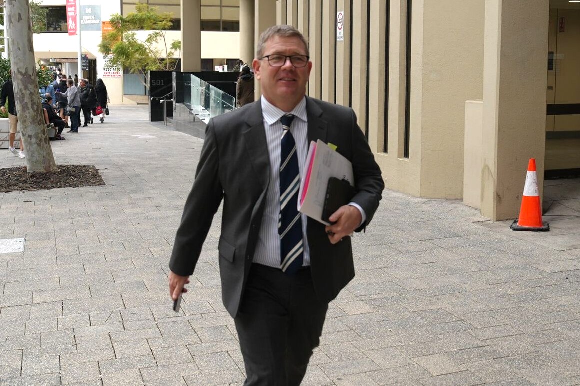 Defence lawyer Michael Tudori walks along a footpath outside the Perth Magistrates Court, wearing a suit and tie.