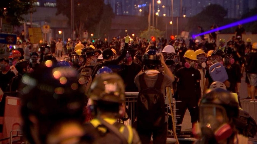 Night show of crowds of protestors on street wearing helmets and gas masks.