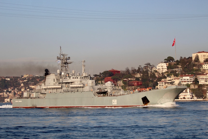 A grey warship floats off the coast of a Turkish city.