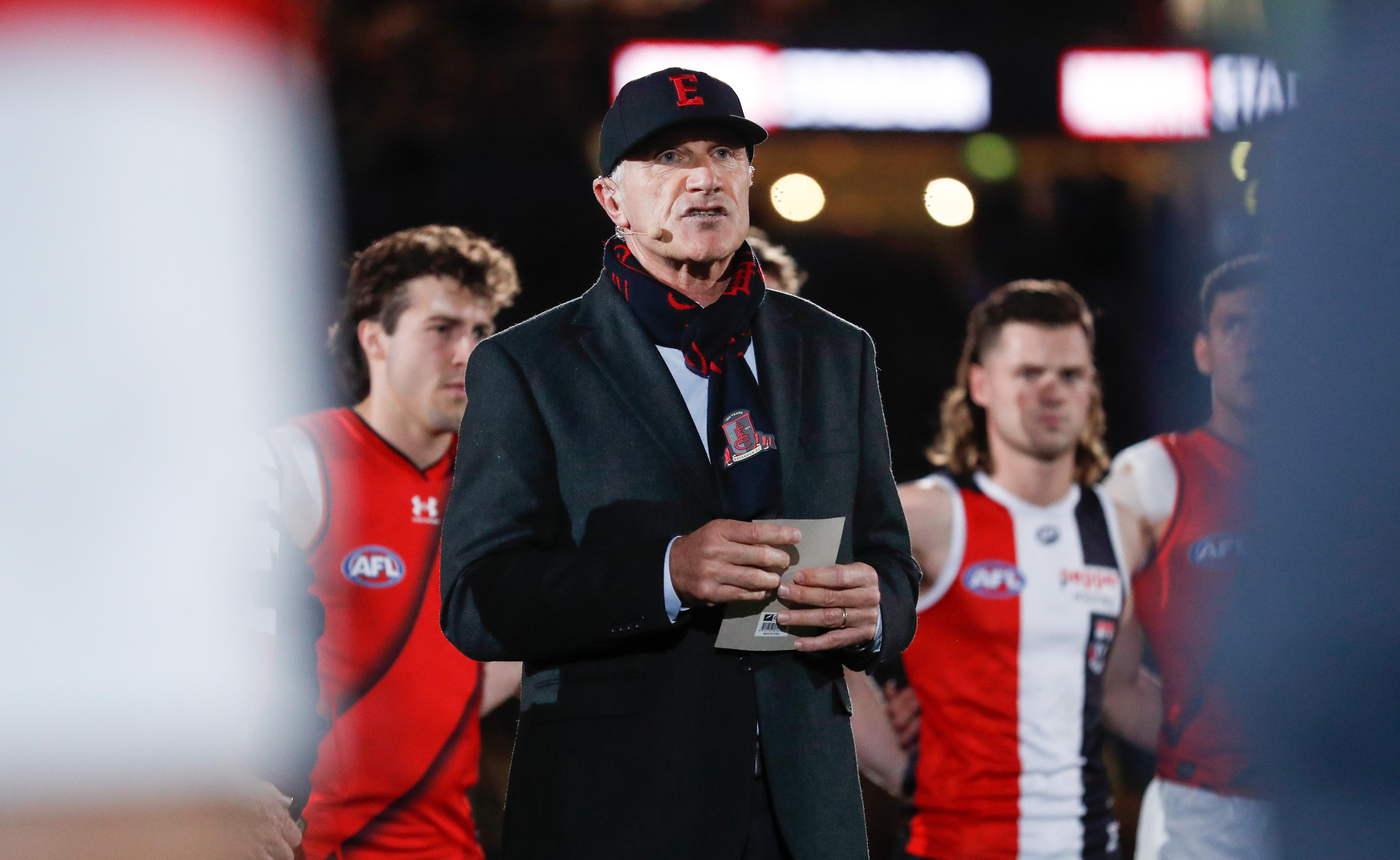 Tim Watson wearing an Essendon cap and hat and speaks
