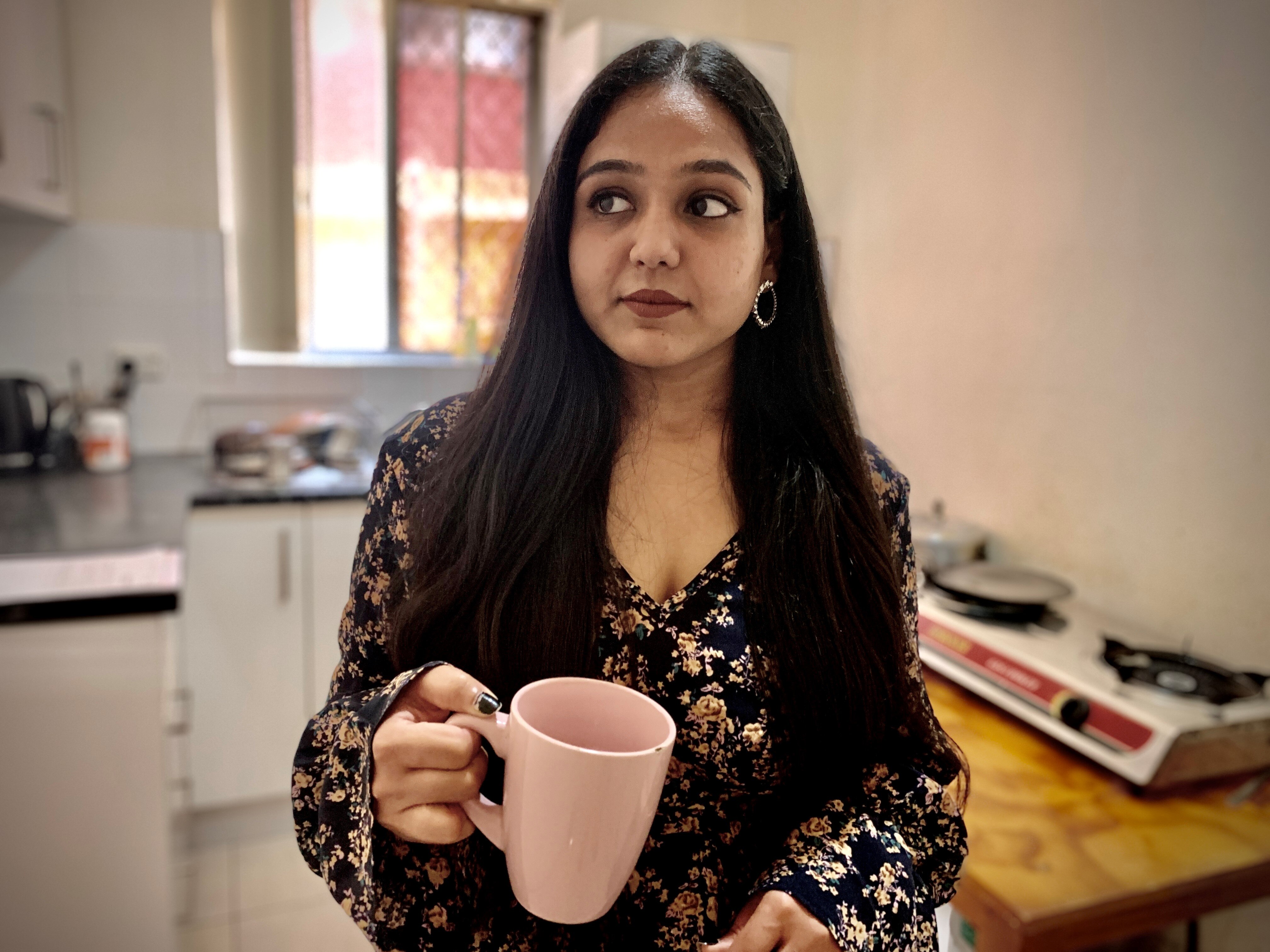 A woman holds a pink mug in the kitchen.