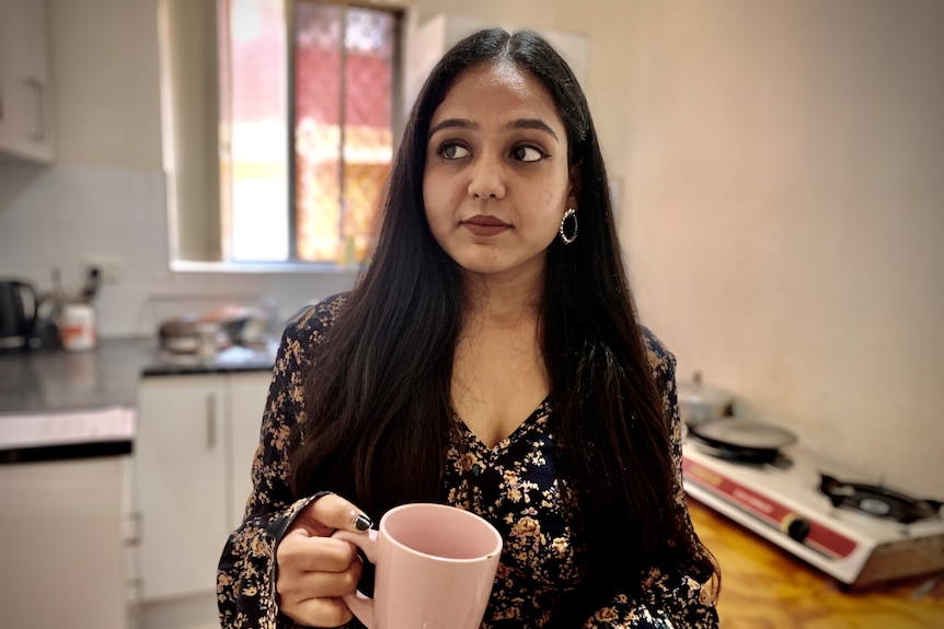A woman holds a pink mug in the kitchen.