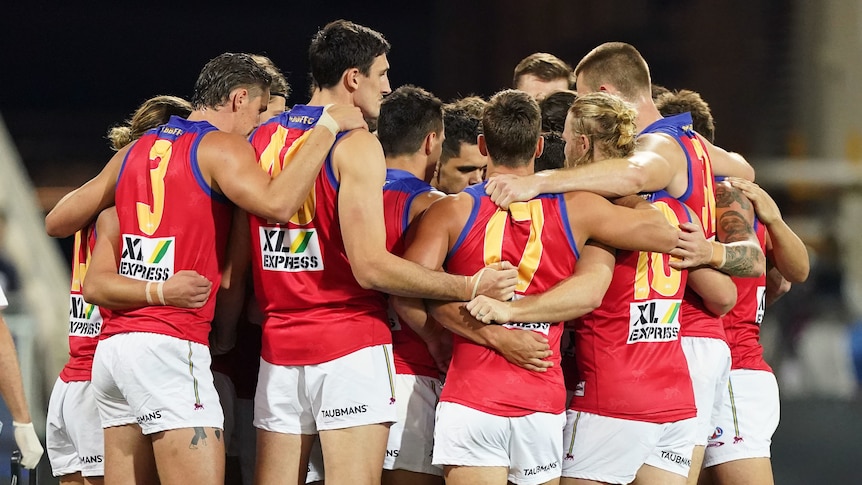 Brisbane Lions players huddle together with their arms linked