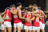 Brisbane Lions players huddle together with their arms linked