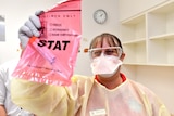 A medical professional holds up swab specimens in a biohazard bag.