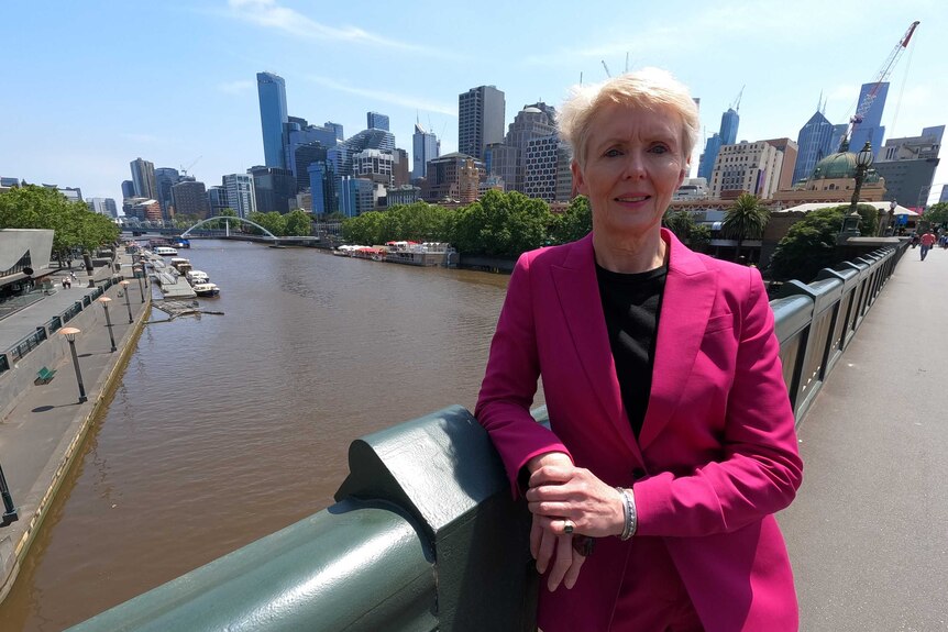 Lady wearing pink suit standing by the bridge with Southbank and the Yarra River in the background.