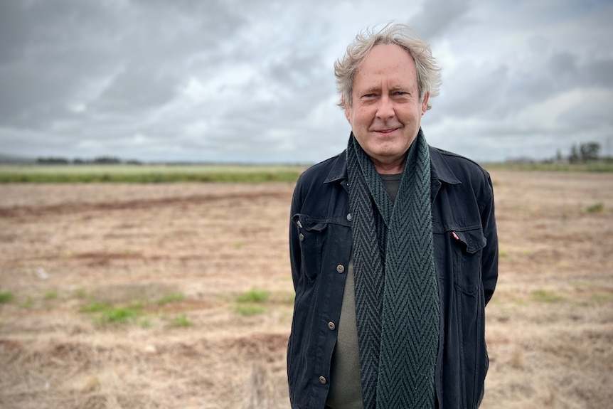 A man standing in front of a dry, grassy landscape wearing dark clothing.