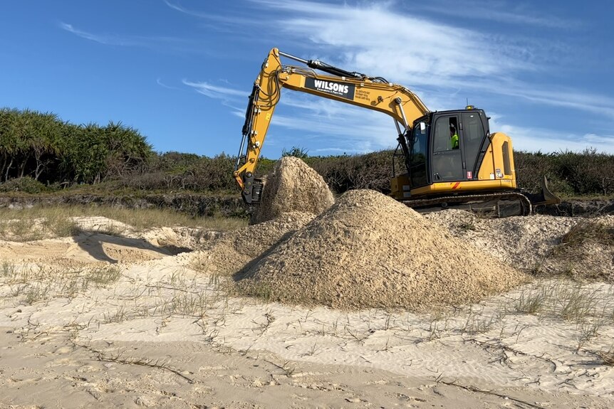 A yellow excavator digging a hole on a beach. 