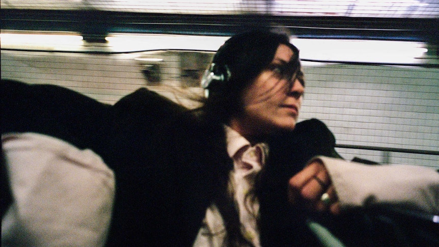 a photo of american dj DOSS, she looks like she's running through a trainstation, she's wearing a suit and headphones
