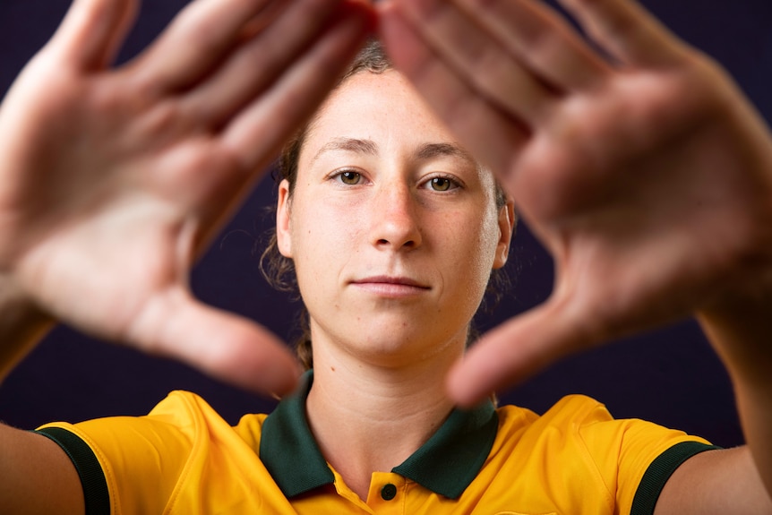 A female soccer player wearing yellow and green holds her hands across a camera lens