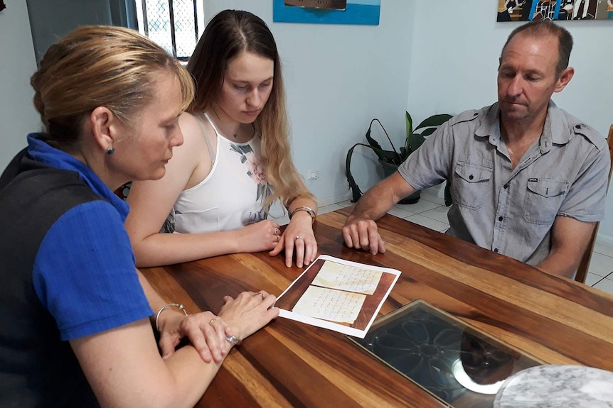 Three people at a table staring at a photo of two letters