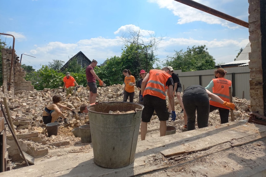 Volunteers in orange vests clear rubble from a destroyed building