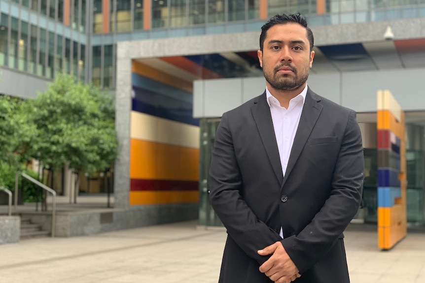 Rohit Karki wears a black suit and stands outside the Federal Court in Melbourne with hands clasped in front of him.