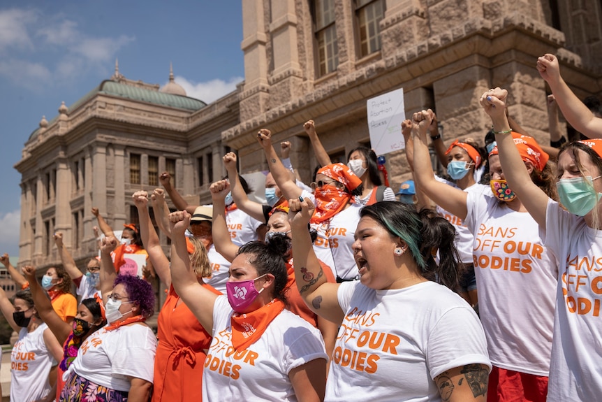 Women dressed in t-shirts saying "bans off our bodies" hold their fists in the air.