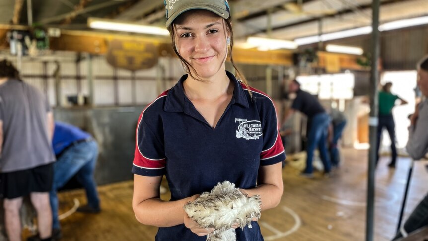 A young girl stands holding wool in a shearing shed