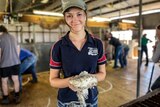A young girl stands holding wool in a shearing shed