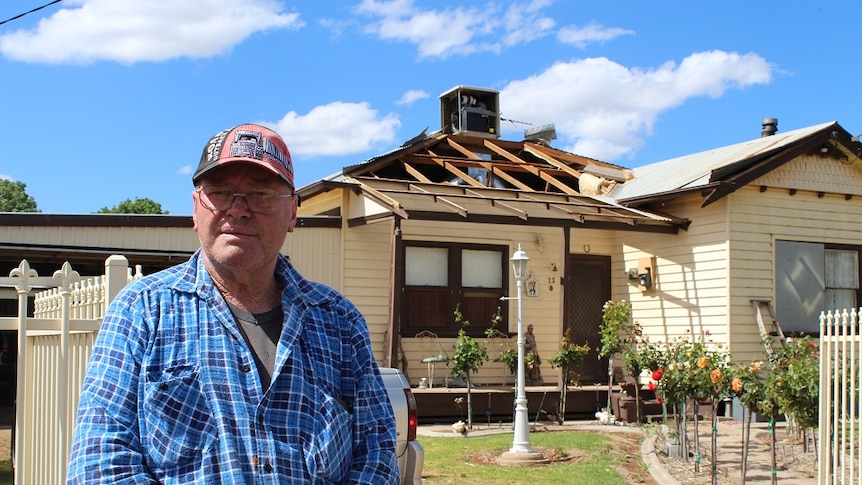 Older man stands in front of house with half of the roof missing.