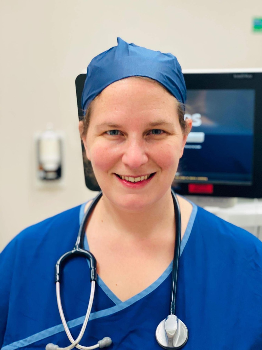 Dr Megan Belot in blue scrubs with a stethoscop3 around her neck and a monitor in the background.