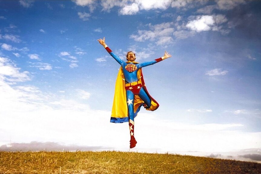 A man wearing a superman type suit jumps in the air