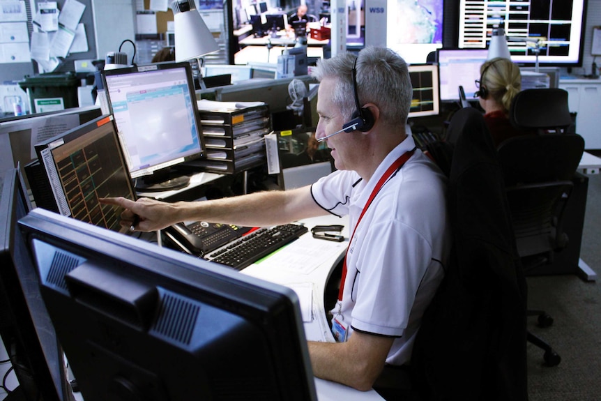 Man with telephone headset on sits at bank of computers