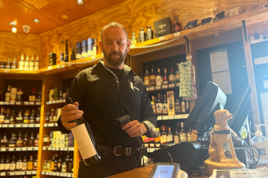 a man standing at the register of a bottle shop scanning a bottle of wine