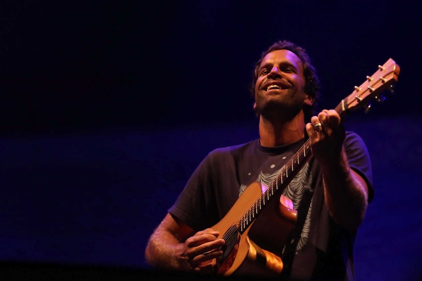 A man with an acoustic guitar performs on stage.
