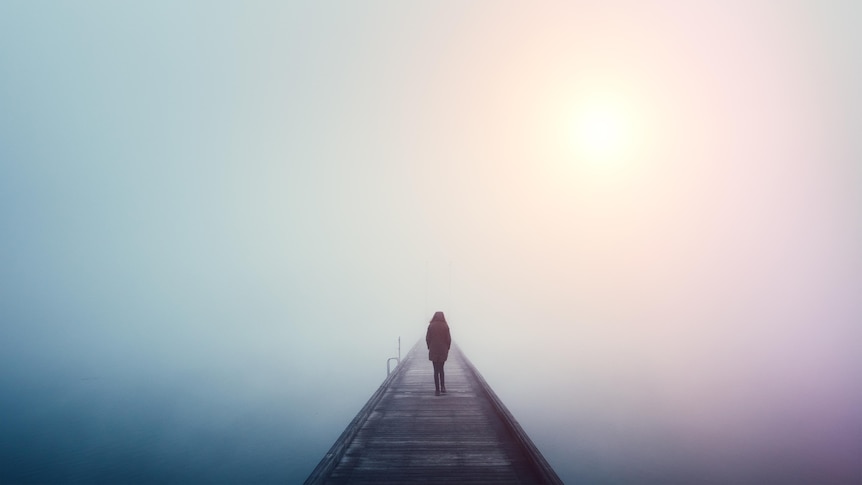 back of woman wearing coat walking on bridge surrounded by fog