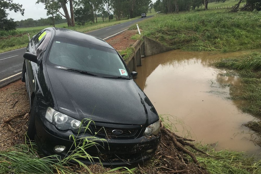 A black sedan is lopsided next to floodwater