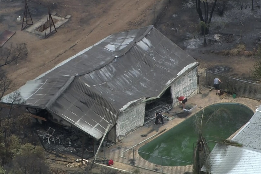 The crumpled remains of a shed as people clean up next to a swimming pool