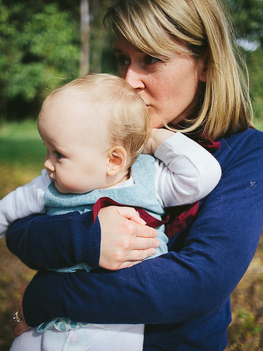Woman with shoulder length brown hair holds her baby and kisses it on the back of its head