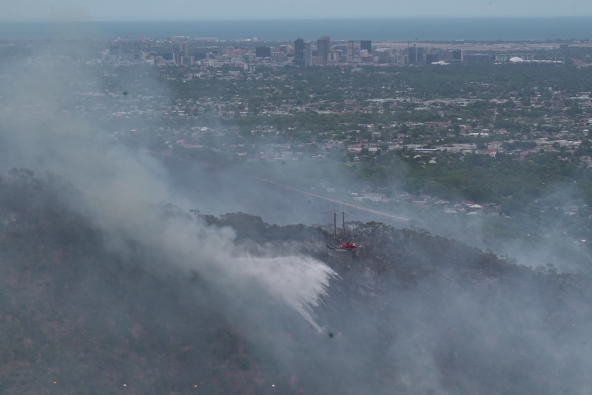 Helicopters pour water on a fire with smoke in front of a city