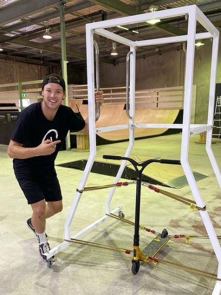 Man in black shirt smiling and standing next to custom-built frame