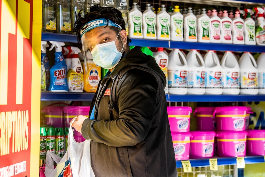 A worker wearing a mask and face shield at a shop in Liverpool stocks shelves.