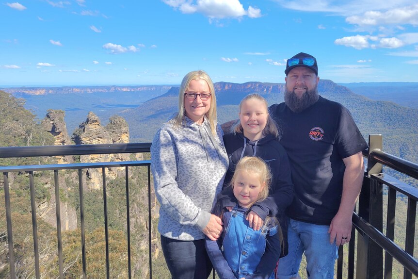 Family of four standing on a lookout with mountains in the background