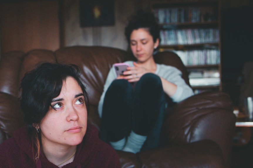 Two women gathered around a couch in a living room.