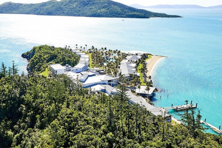 Resort buildings on a tropical island surrounded by light blue water.