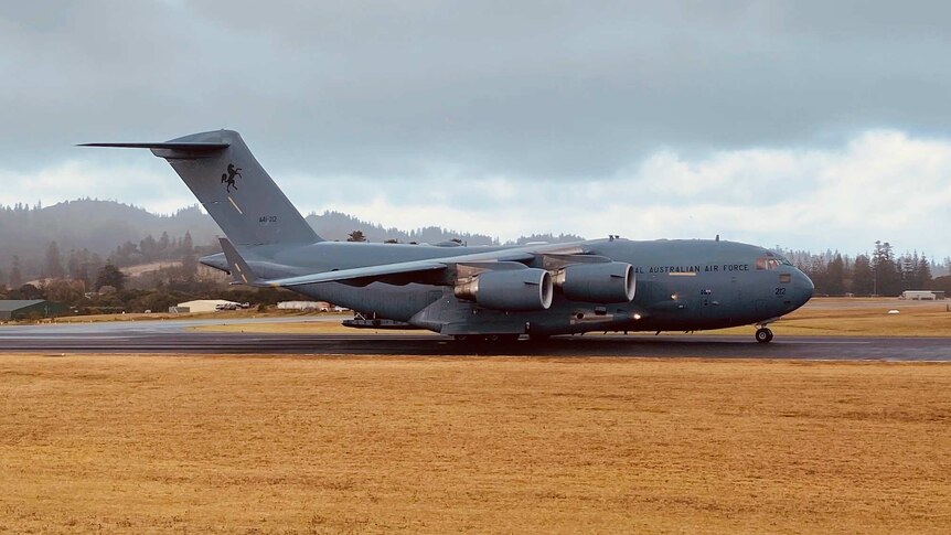 A grey military plane landing on an air strip.