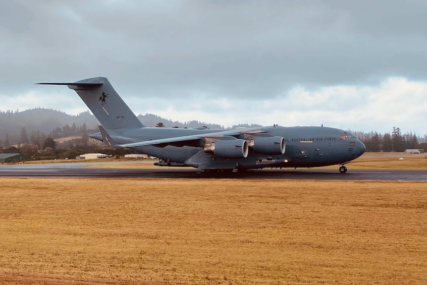 A grey military plane landing on an air strip.