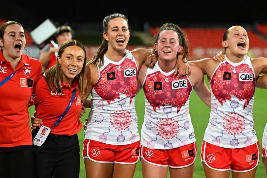 Sydney Swans players stand arm in arm smiling.
