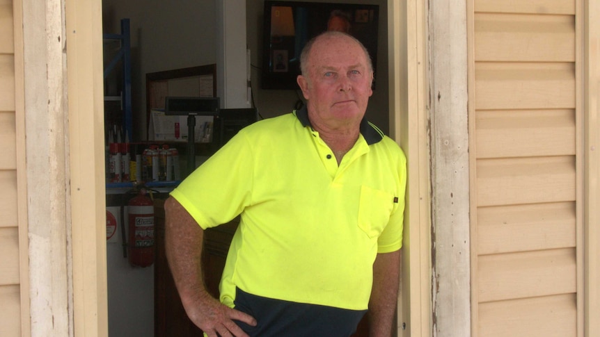 A man in a yellow high visibility shirt leans in a doorway looking at the camera.