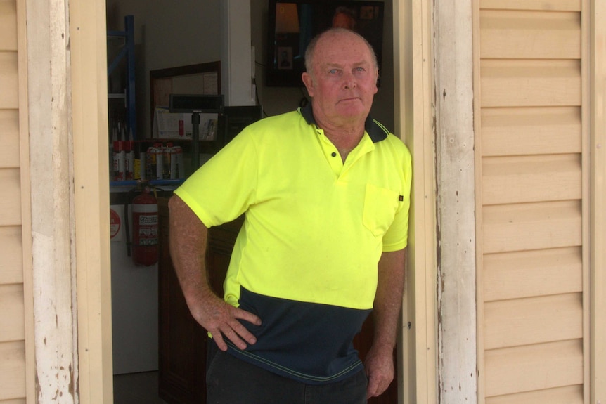 A man in a yellow high visibility shirt leans in a doorway looking at the camera.